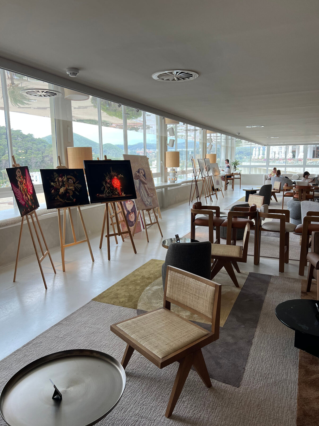 Easels along the panoramic windows — Ibiza skyline beyond.