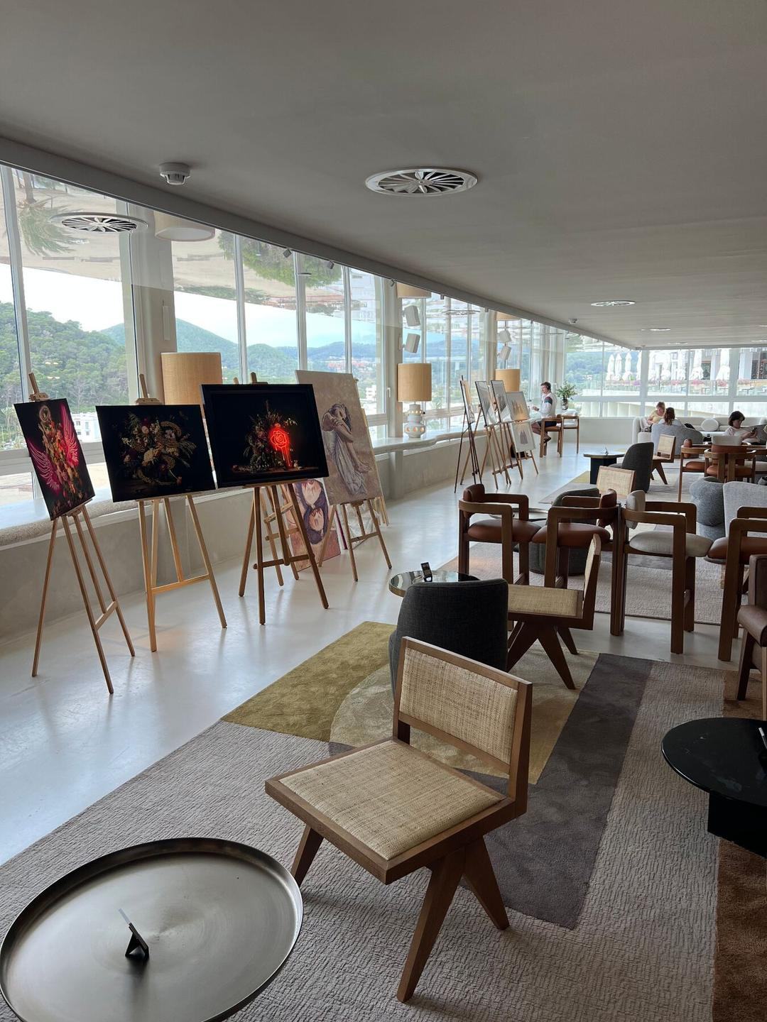 Easels along the panoramic windows — Ibiza skyline beyond.